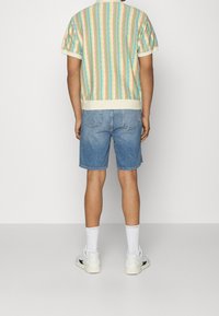 Randig t-shirt i pastellfärger med ribbad mudd, tillsammans med blå jeansshorts och vita sneakers med svarta detaljer.
