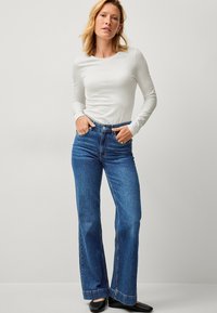 Witte lange mouwen top gecombineerd met blauwe high-waisted flared jeans. Gestructureerde denimstof, met een klassiek vijf-pocket ontwerp en beige stiksels.
