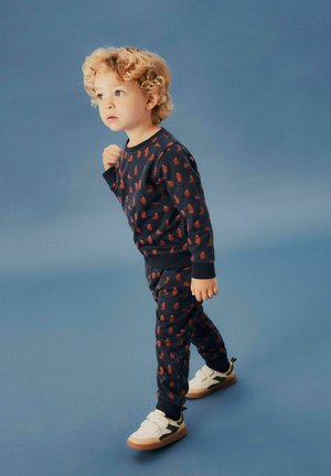 Chándal infantil azul marino con un patrón repetido de osos, hecho de tela suave. Combinado con zapatillas blancas con acentos grises.