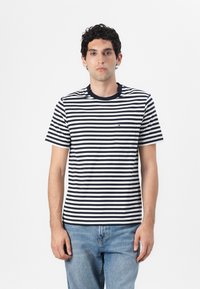 Navy and white striped cotton t-shirt with a crew neckline and short sleeves; features a pocket on the left chest. Worn with light blue jeans.