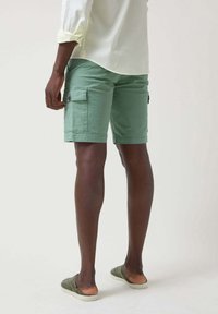 Pantalones cortos cargo verdes de tejido ligero, con bolsillos laterales y un corte recto, combinados con zapatos ligeros tipo slip-on.