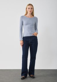 Light blue long-sleeve top with a round neckline, paired with dark blue flared jeans. The jeans feature front pockets and a classic design.