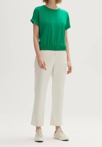 Grøn kortærmet top med elastisk talje parret med hvide, lige ben bukser. Sættet fuldendes med lyse sneakers.