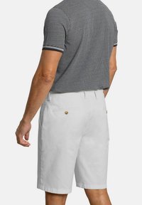 Bermudas de algodón blancas con un corte relajado, que cuentan con bolsillos traseros con botones color crema y una textura suave, combinadas con una camiseta polo de rayas en color marino.