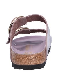 Vista posteriore di un sandalo con due cinturini in suede rosa e accenti circolari dorati, una soletta in sughero e una suola in gomma nera con texture.