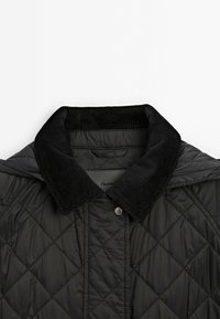 Zwarte gewatteerde jas met een corduroy kraag. Heeft een ruitpatroon, drukknoopsluiting en een gladde textuur.