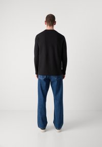 Camisa negra de manga larga combinada con unos vaqueros de pierna ancha en azul claro. El conjunto presenta líneas simples y limpias con un ajuste casual.