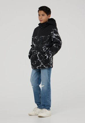 Giacca con cappuccio a motivo marmorizzato in bianco e nero, con tasche con zip, abbinata a jeans strappati blu e sneaker bianche.