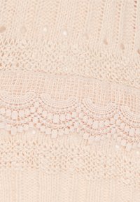 Tessuto a maglia in morbido rosa con texture a coste, caratterizzato da eleganti dettagli in pizzo e un motivo ondulato lungo le cuciture orizzontali.