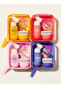 Quatre coffrets de soins de la peau, format voyage, colorés, comprenant un gel douche, une crème et un spray d’huile dans des pochettes transparentes jaunes, rouges, roses et bleues.