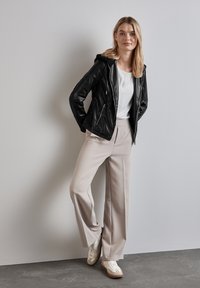 Giacca nera in finta pelle con cappuccio, blusa bianca, pantaloni beige a gamba larga e sneaker color crema. Texture liscia con dettagli della cerniera frontale.