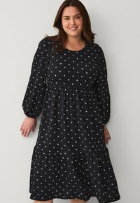 Vestido negro con lunares, mangas largas y globosas, falda en capas, escote redondo, hecho de una tela ligera con un acabado texturizado.