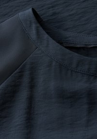 Marineblauwe stof met een gladde textuur en subtiele glans. Beschikt over een ronde halslijn en een contrasterend paneelontwerp op de schouders.