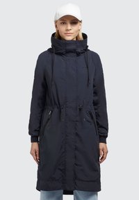 Marineblå lang parka-jakke med høj krave, snøre i taljen og to lynlåslommer i siden. Fremstillet af letvægts, vandafvisende materiale.