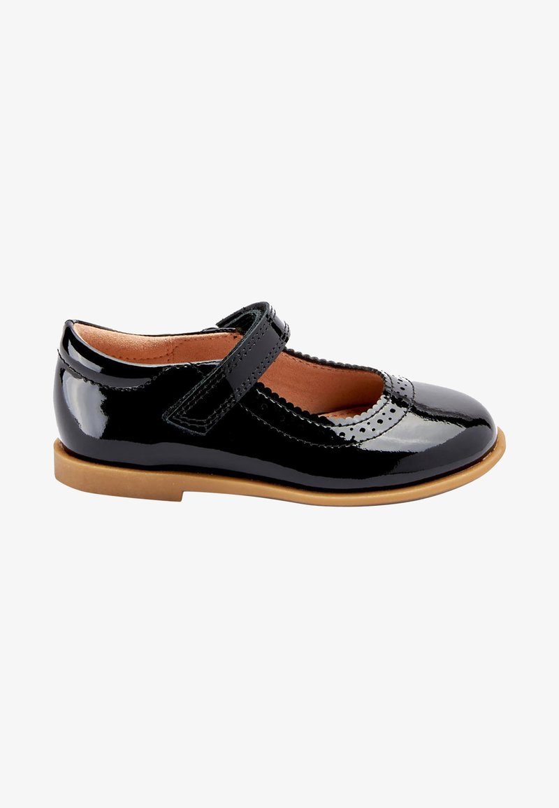 Chaussure Mary Jane en cuir verni noir avec des détails festonnés et une sangle Velcro. Semelle plate couleur tan, bout arrondi et finition lisse.