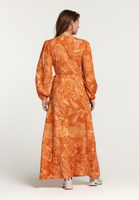 Lang oranje jurk met bloemmotief, met lange mouwen, een getailleerde taille en een vloeiende rok. Geweven stof en subtiele details zijn zichtbaar.