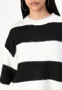 Black and white striped knit sweater with a soft texture. Features a crew neckline and wide horizontal bands, emphasizing contrast.
