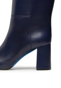 Stivale alla caviglia in pelle blu navy con tacco a blocco, texture liscia e fodera blu a contrasto. Presenta cuciture visibili e punta arrotondata.
