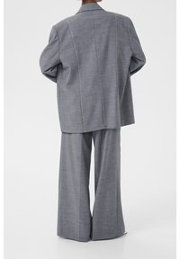 Harmaa räätälöity ylikokoinen bleiseri ja leveälahkeiset housut teksturoidusta kankaasta, joissa valkoiset tikkauskoristeet saumoissa.