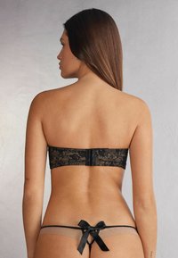 Black lace strapless bra with floral pattern and silicone underwire, paired with mesh and satin bikini bottom featuring a bow detail.