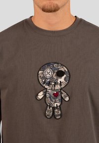 Hnědá dlouhá rukávová košile se vyšitým designem postavy v modré a stříbrné barvě s červeným srdíčkem. Texturovaná látka, kulatý výstřih.