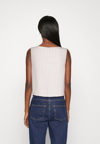 Utan ärmar, kort topp i ljusbeige med vertikala ränder, kombinerad med mörkblå jeans. Slät textur, enkel design och rakt skuren.