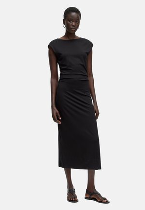 Robe midi noire ajustée avec des manches courtes, détail froncé sur le côté et texture douce. Assortie avec des sandales noires plates.