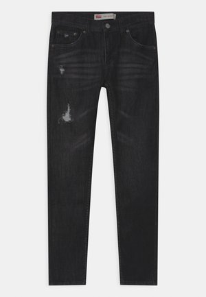 Jean skinny noir avec légère usure sur la cuisse gauche et la poche, fermeture avant à boutons, et conception à cinq poches.