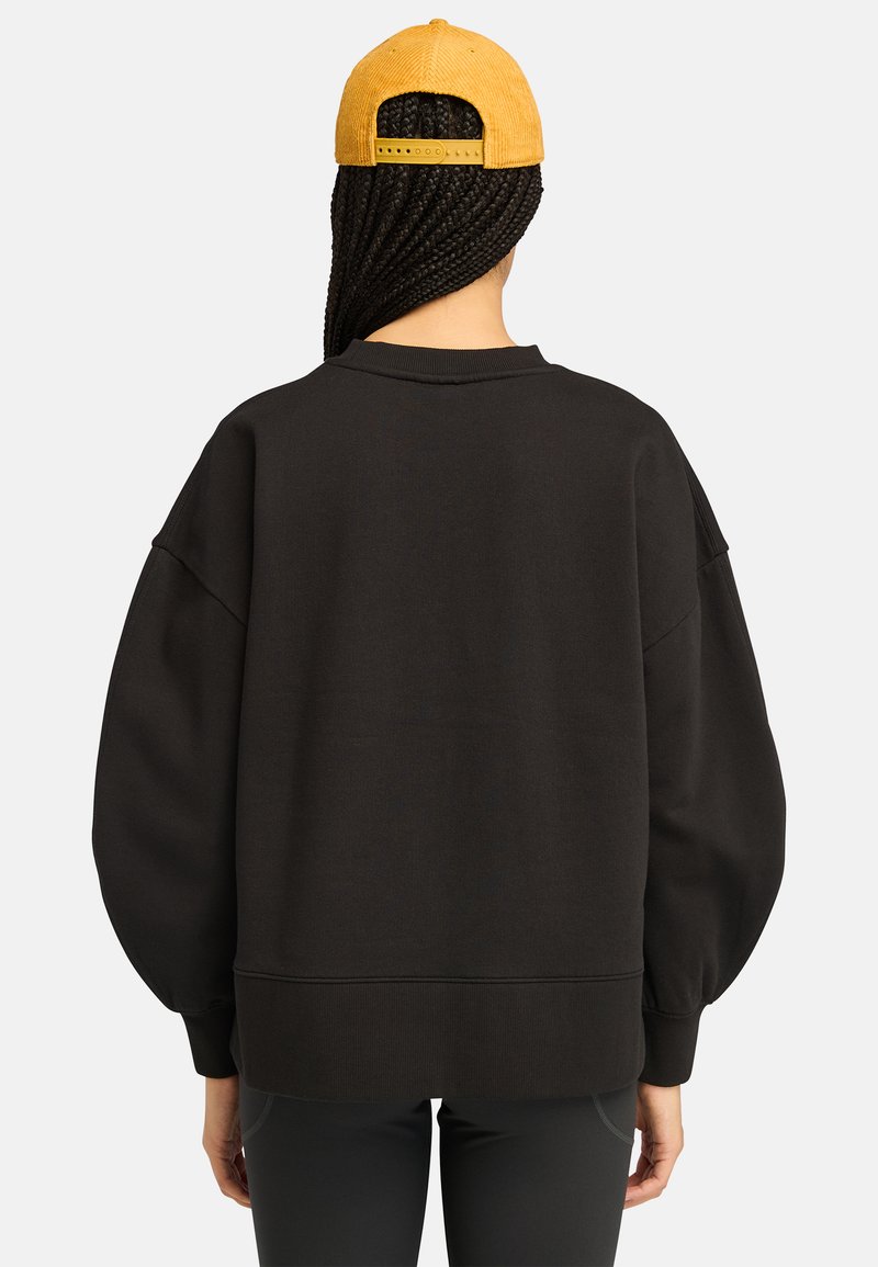 Felpa nera oversize con spalle scese, polsini e orlo a costine. Abbinata a un berretto giallo in corduroy, dotato di una cintura regolabile sul retro.
