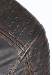 Braunes Lederpolster mit gestepptem Textur, das kontrastierende braune Nähte und eine leicht abgenutzte Optik aufweist. Abgerundete Form am Rand.