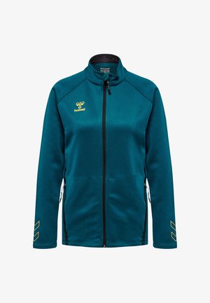 Sportowa kurtka teal z pełnym zamkiem błyskawicznym i stójką, żółte logo hummel na piersi oraz wzory w kształcie szewronów na rękawach, zapinane na zamek kieszenie boczne.
