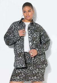 Giacca con stampa leopardata in tonalità grigie, realizzata in tessuto resistente; abbinata a una gonna coordinata, con bottoni e tasche. Dettagli ad anello visibili.