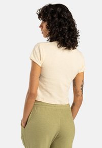 Cream short-sleeve cropped t-shirt with rolled cuffs, paired with light green elastic waist pants. Fabric appears soft with a casual fit.
