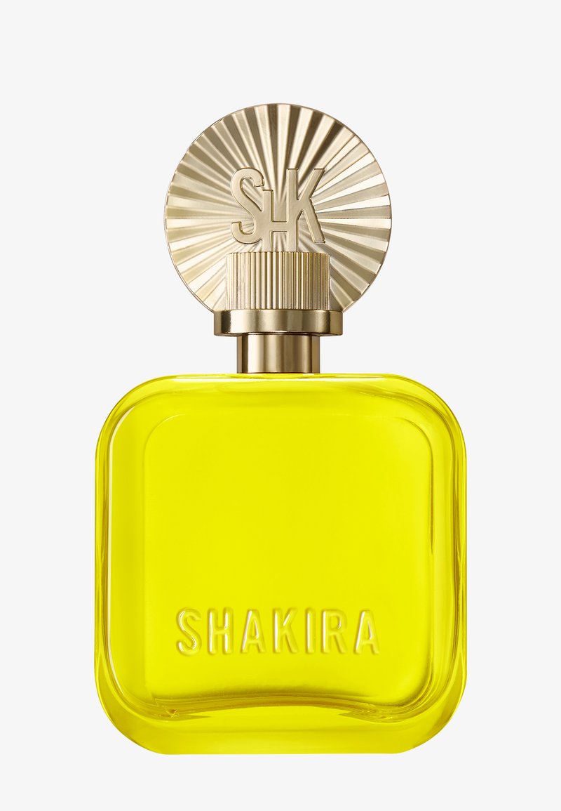 Gul firkantet parfymeflaske med avrundede kanter, preget "SHAKIRA"-tekst og en gull farget rillede rund hette med solstrålemønster og "SK"-initialer.