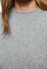 Pull en tricot gris avec un col rond, présentant une texture douce et un motif légèrement chiné sur l'ensemble. Design minimaliste, sans matériel visible.