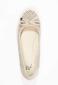 Ballerine beige perforée avec un petit nœud et une semelle intérieure rembourrée, photographiée vue de dessus sur fond blanc.