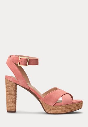 Różowy zamszowy sandał na wysokim obcasie z paskiem wokół kostki z klamrą, plecioną platformą i szerokim obcasem na jednolitym jasnym tle.