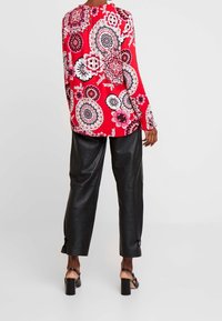 Blusa roja de manga larga con patrón floral, combinada con pantalones de cuero negros holgados y sandalias de tacón cuadrado negras, vista desde la parte posterior.