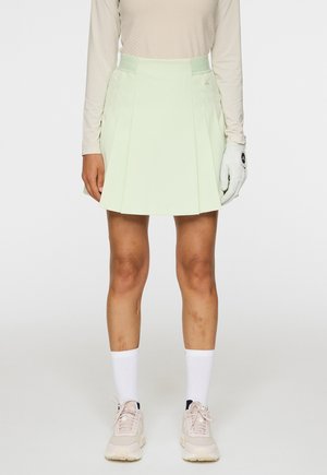 Ljusgrön golfkjol med veck, tillverkad av ett mjukt material. Kombinerad med en långärmad beige topp och vita strumpor, vilka har mjuka rosa sneakers.