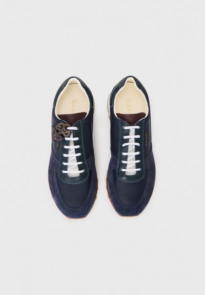 Navy and dark green sneakers feature a suede toe, leather accents, white laces, and a floral design on the side. Rubber sole.