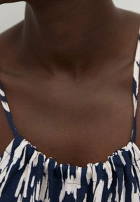 Blue and white patterned fabric with gathered neckline and narrow straps, showing smooth skin tone and collarbone.