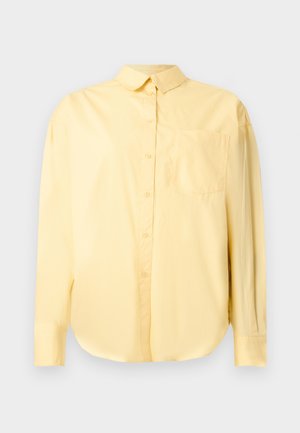 Pikkade varrukatega kahvatu kollane nööpidega särk, millel on krae ja rinnatasku, esitatud ühetaolise heleda tausta vastu.