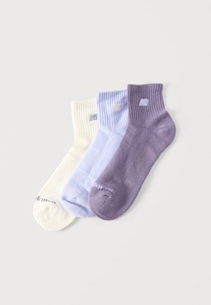 Drei Knöchelsocken in Creme, Hellblau und Lavendel mit gerippten Bündchen und kleinen Logos an Bündchen und Zehen, nebeneinander ausgelegt.
