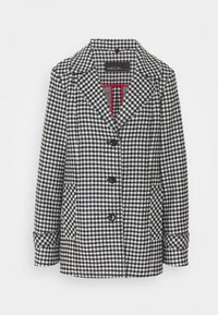 Sort-hvid hundetandsmønstret blazer med spids revers, to forlommer og fire sorte knapper. Har en rød accent indvendig foring.