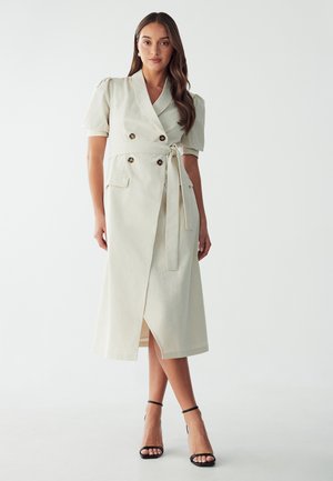 Light beige, knee-length dress with a double-breasted design, short puff sleeves, tie waist, and front slit; features button accents and side pockets.