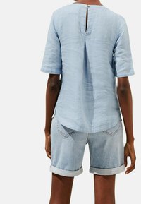 Ljusblå, kortärmad topp med subtil randig textur och öppning med nyckelhål bak, i kombination med denimshorts med uppvikta fållar.