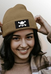 Brown ribbed beanie with black patch featuring a white skull and crossed bones. Soft material and snug fit, ideal for casual wear.