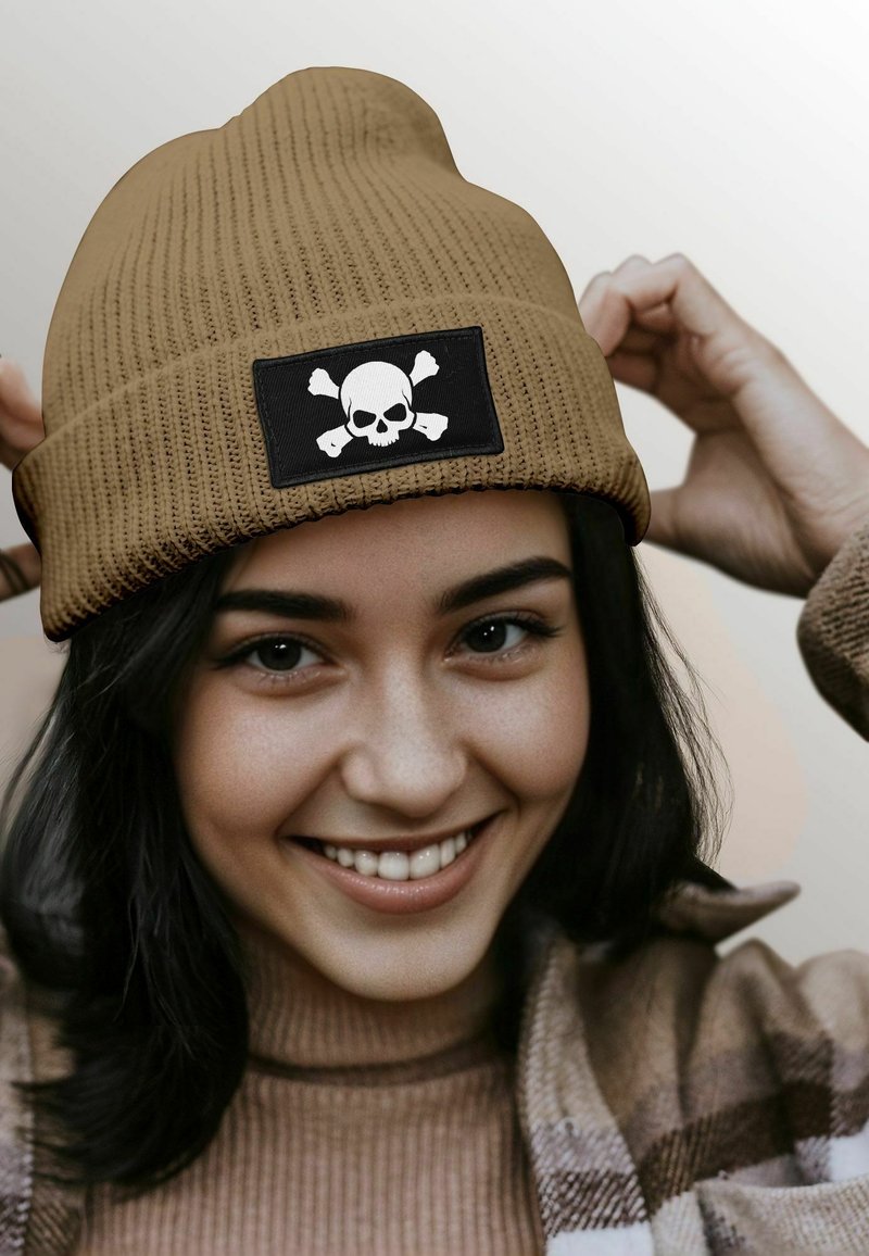 Brown ribbed beanie with black patch featuring a white skull and crossed bones. Soft material and snug fit, ideal for casual wear.