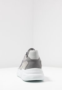 Baskets en daim gris avec une semelle blanche et des accents gris brillants. Elles disposent d'un col rembourré et d'une texture lisse sur le talon.