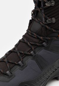 Czarne buty robocze z teksturowaną cholewką, wzmocnionym noskiem oraz kontrastowymi pomarańczowymi akcentami w sznurowadłach i przeszyciach.